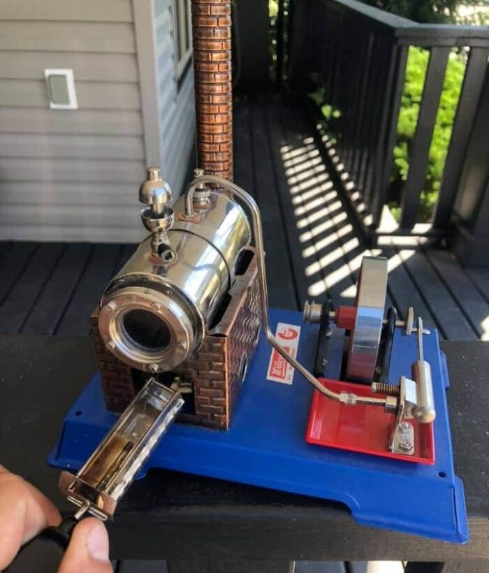 Miniature old steam engine model with metal and brick details on a blue base, found but unknown to owner initially.