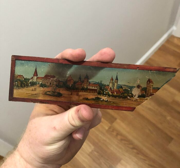 Hand holding a small vintage painted fragment depicting an old town scene, found as a mysterious old object.