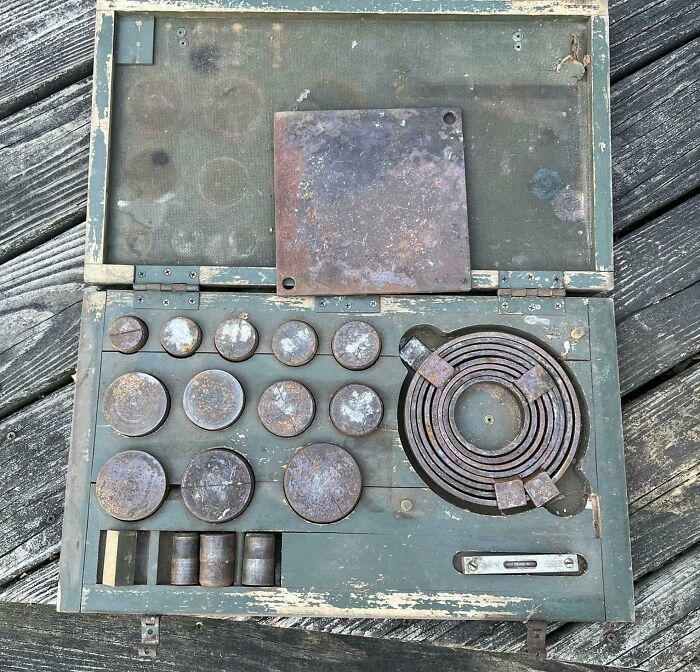 Old mysterious metal objects arranged in a weathered green wooden box found by people with no clue.