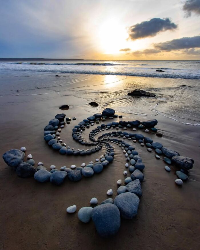 Hypnotic land art made of spiraled stones on a beach at sunset, showcasing Jon Foreman's Wales beach sculpture.