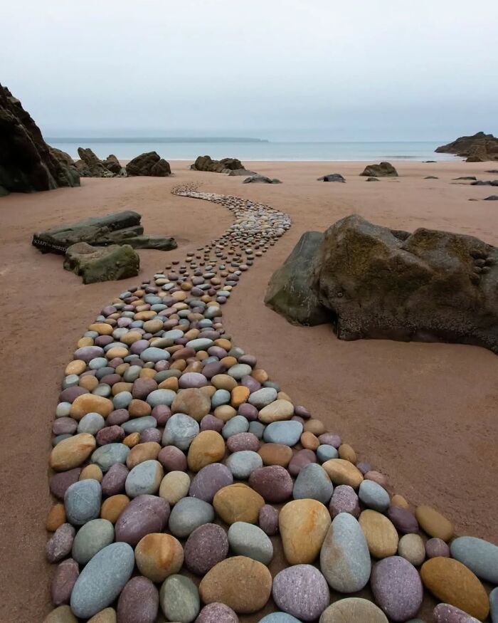 Colorful stones arranged in a winding path on a sandy beach, showcasing hypnotic land art on Wales’s coastline.