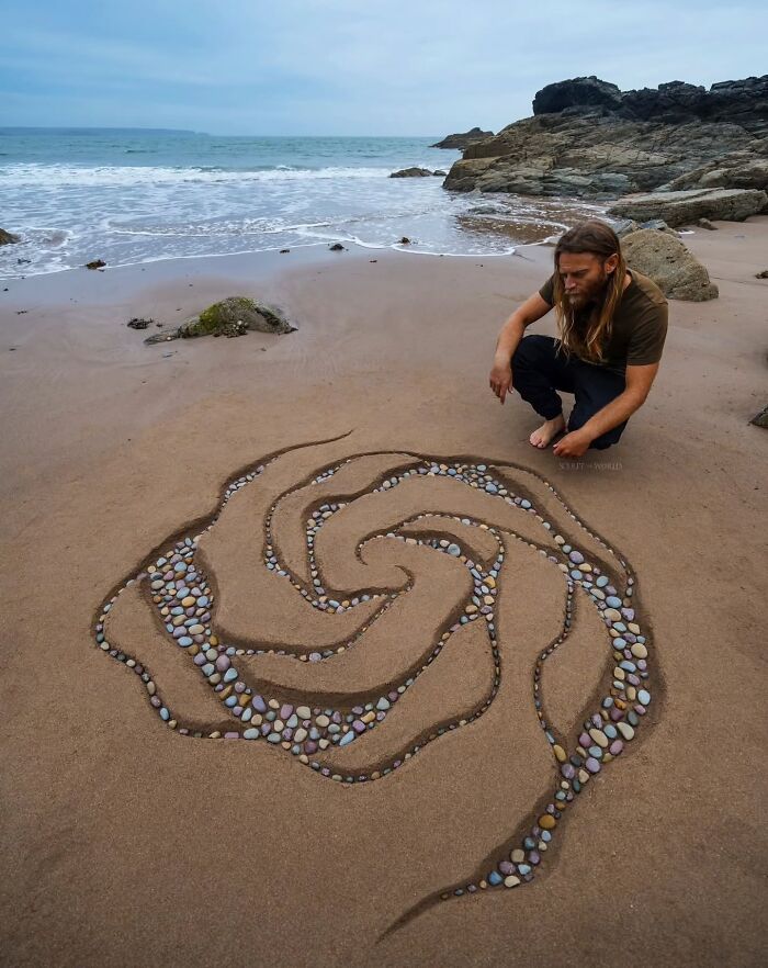 Man crouching by hypnotic land art made of stones and sand on a beach in Wales, sculpting nature-inspired shapes.