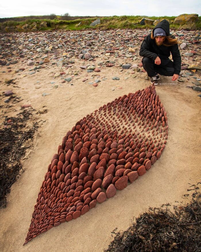 Artist Jon Foreman arranging hypnotic land art made of red stones on a sandy beach in Wales, part of Sculpt The World.
