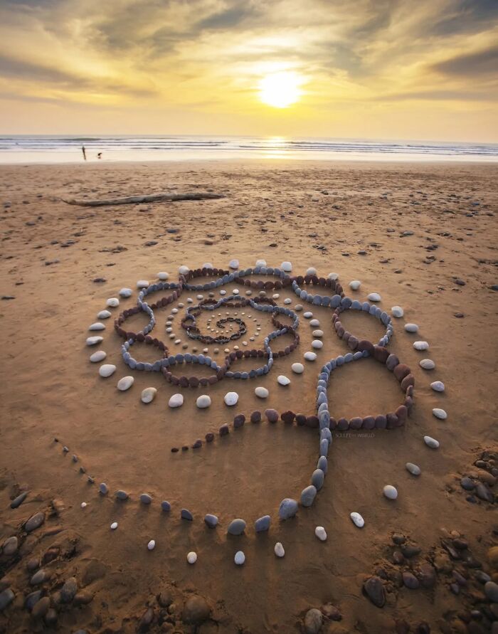 Spiral land art made of stones on a sandy Wales beach at sunset, part of Jon Foreman’s hypnotic land art series.