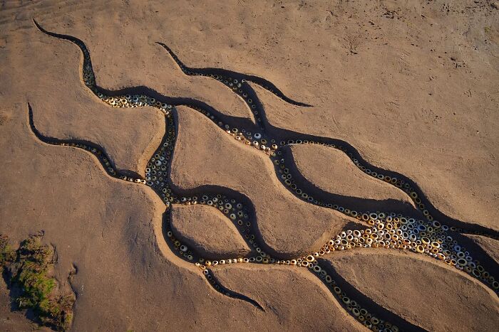Land art sculpture on a sandy beach in Wales featuring winding patterns filled with circular objects by Jon Foreman.