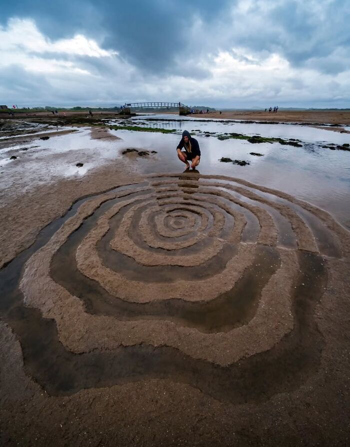 Jon Foreman creating hypnotic, short-lived land art sculpture on a sandy beach in Wales under a cloudy sky.