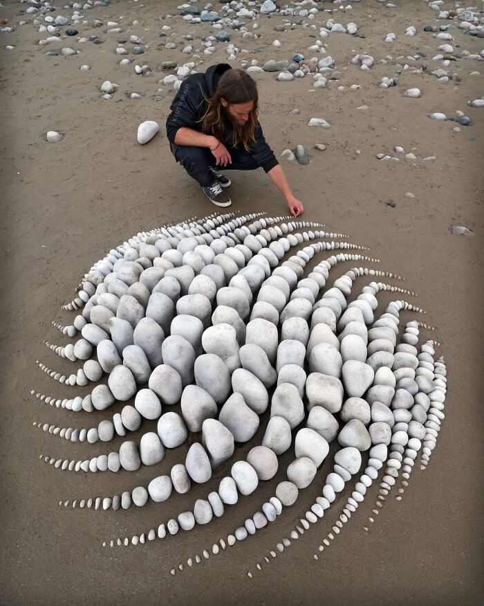 Artist Jon Foreman creating hypnotic land art with white stones arranged on a sandy beach in Wales.