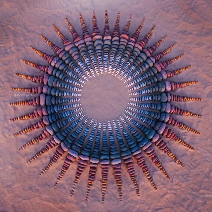 Hypnotic land art made of carefully stacked stones arranged in a circular pattern on a sandy beach in Wales.