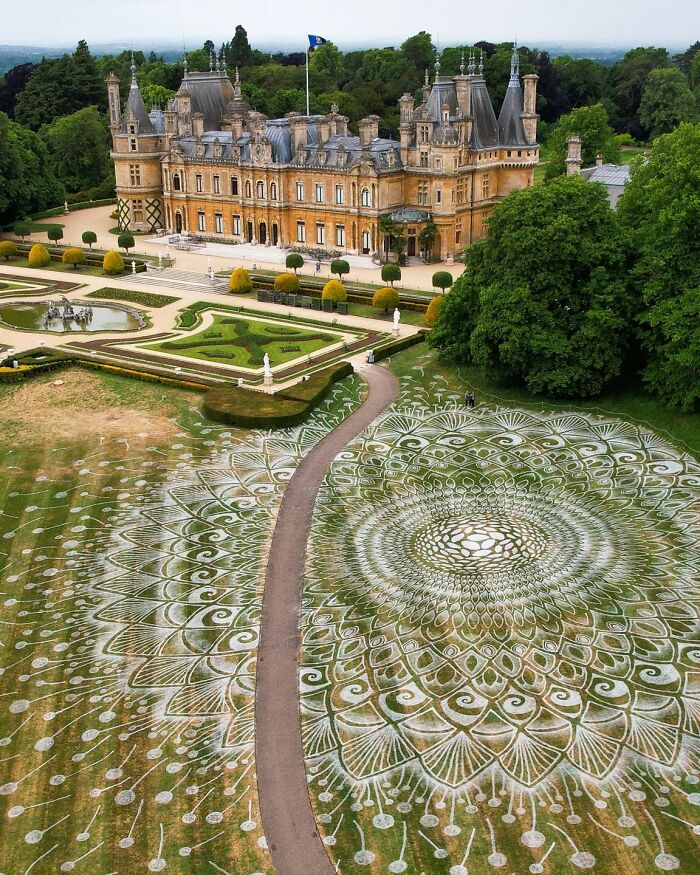 Large intricate land art design on grass near a historic mansion, showcasing hypnotic sculpt the world style patterns.