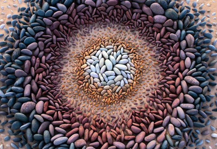 Concentric circle land art made of colorful stones on a beach, showcasing hypnotic, short-lived sculpture by Jon Foreman.