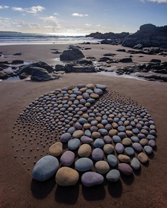 Hypnotic land art made of colorful stones arranged on a sandy beach in Wales, showcasing short-lived nature of sculptures.