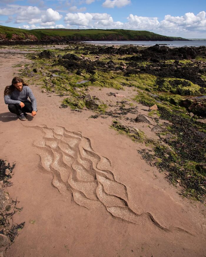 Artist Jon Foreman creating hypnotic short-lived land art sculpture on a sandy beach in Wales with rocky coastline background.