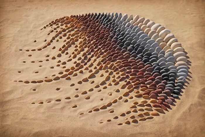 Land art on a sandy beach made of smooth, colorful stones arranged by Jon Foreman in Wales.
