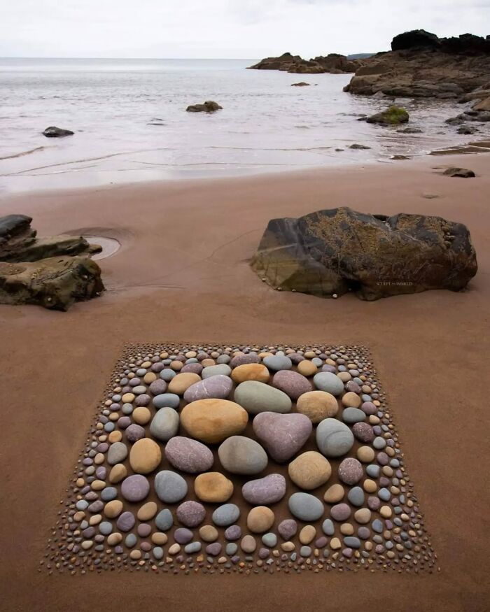 Hypnotic land art on Wales’s beach featuring sculpted arrangement of colorful stones in square pattern on sand.