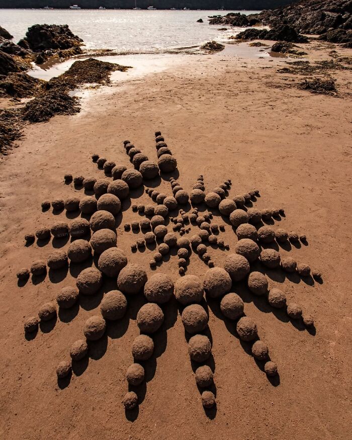 Hypnotic land art made of sculpted sand spheres arranged in a pattern on a quiet beach in Wales.