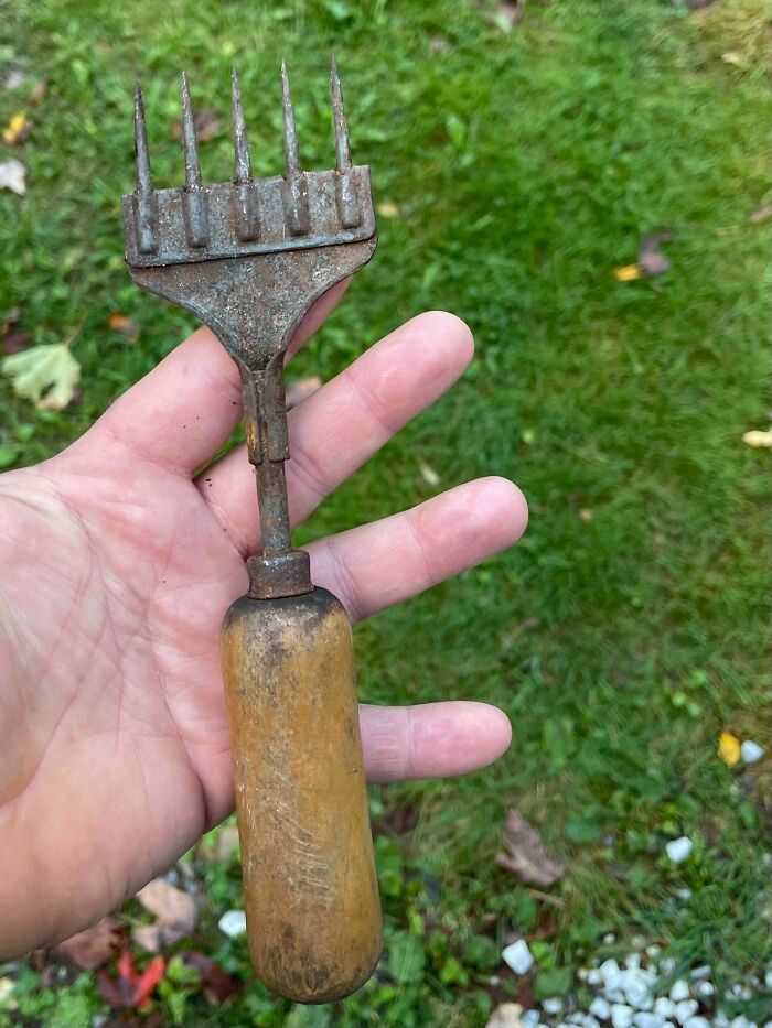 Hand holding an old rusty tool with wooden handle and metal prongs, found but unclear what it is used for.