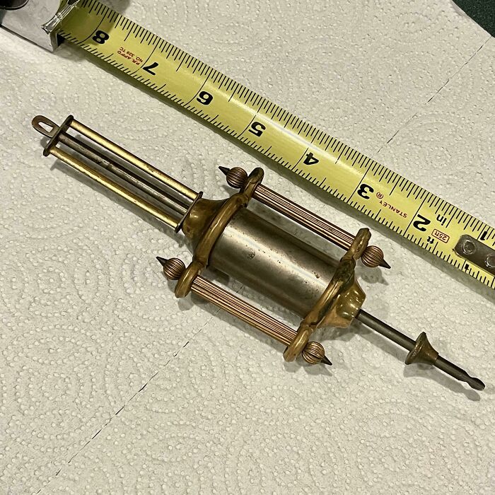 Old mysterious brass object measuring about six inches, found and unidentified, with a yellow tape measure nearby for scale