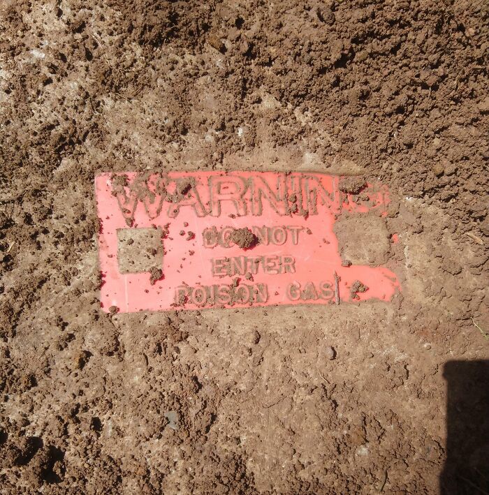 Warning sign partially buried in dirt indicating poison gas, an old protective marker found with no clear identification.