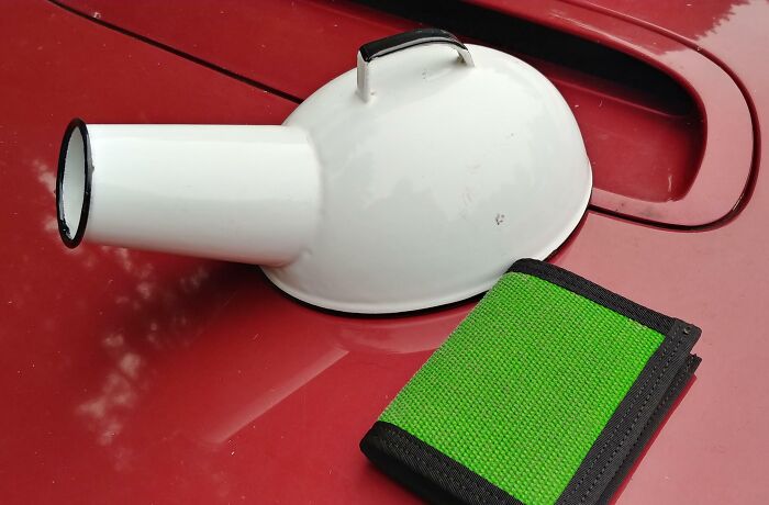 Old white funnel with handle placed on a red surface next to a green wallet, found but no clue what it is.