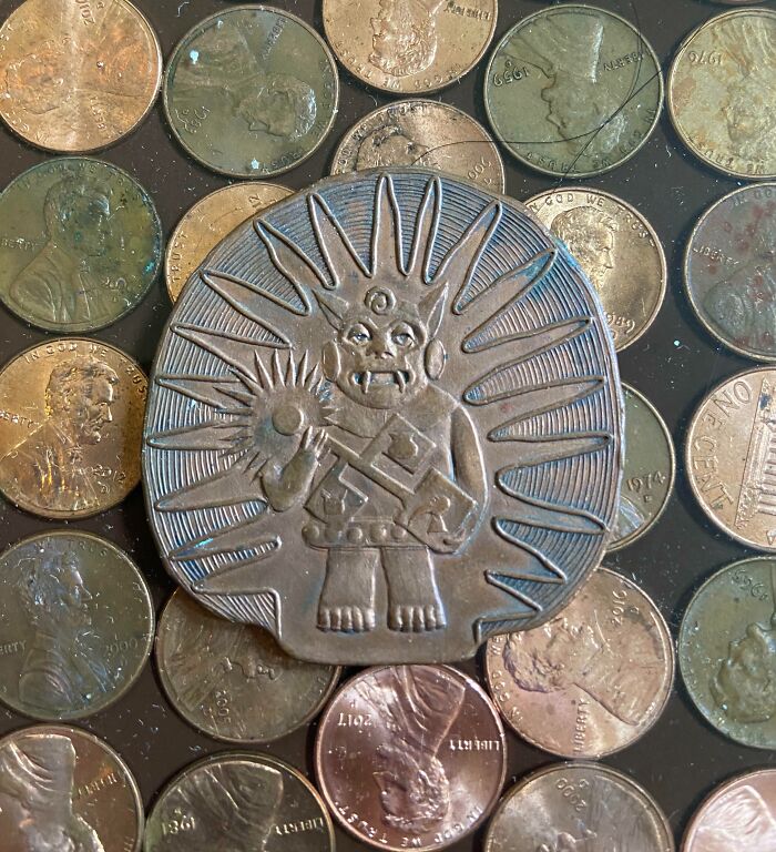 Old artifact with sunburst design placed among scattered vintage US pennies, highlighting unique ancient find mystery.