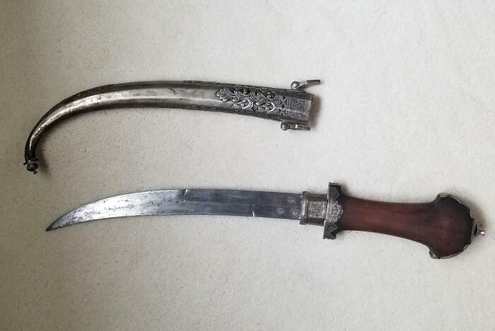 Old curved dagger with ornate metal sheath and wooden handle, found as something old with unknown purpose.