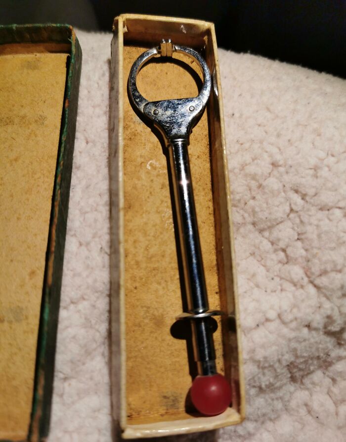 Old metal tool with a red k**b in a vintage box, found among forgotten items needing identification and internet help.