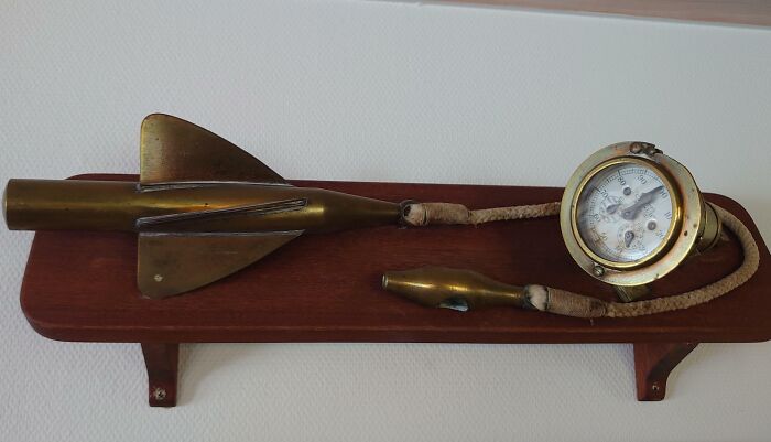 Old brass diving depth gauge and metal tool displayed on a wooden stand, found object with unknown purpose.