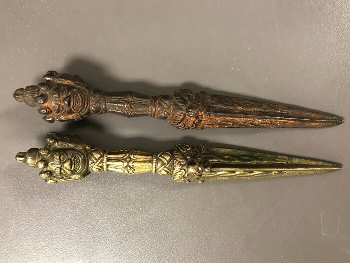 Two ornate old metal objects with detailed faces and intricate designs, found but unidentified by people.