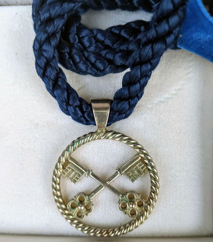 Close-up of an old, vintage pendant with crossed keys on a twisted metal circle and a blue braided cord necklace.