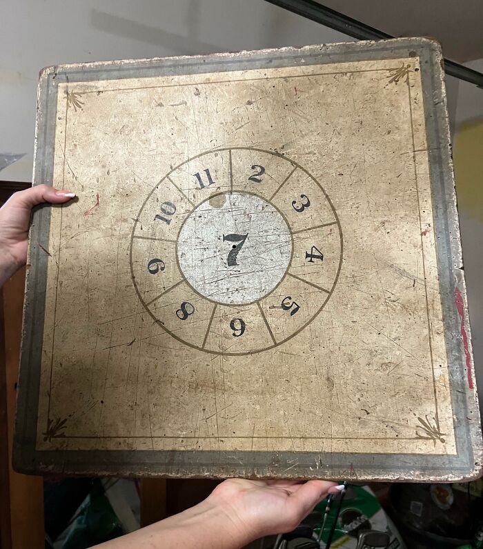 Hands holding an old, worn wooden board with a circular numbered design, an example of something old found online.