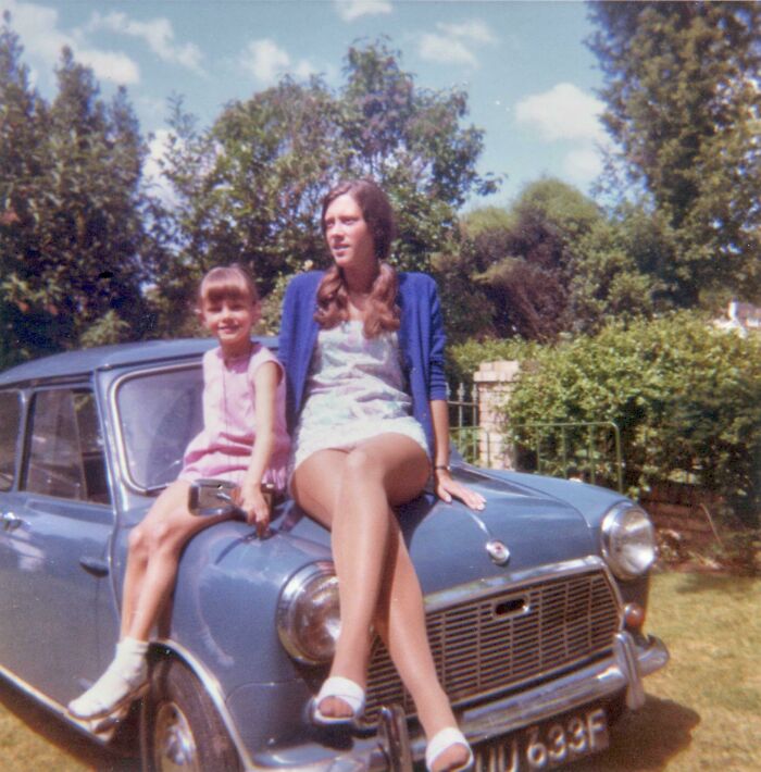 Two girls sitting on the hood of a vintage car in a sunny garden captured in vacation pics before cell phones had cameras.