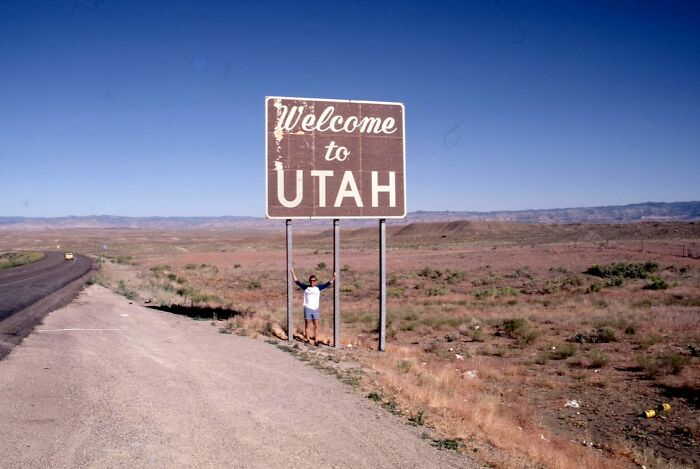 Person standing with arms raised under a Welcome to Utah sign in a vintage vacation pic from before cell phone cameras.