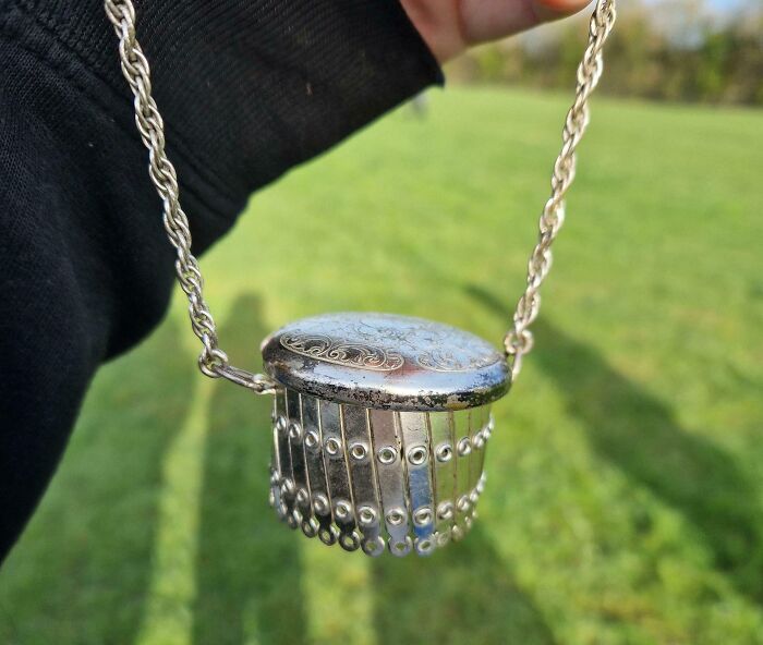 Hand holding an old vintage silver pendant with intricate details found outdoors with grass background.