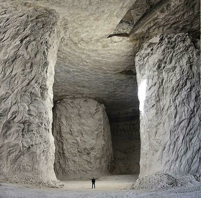 Person standing inside a massive cave, illustrating human for scale and the unusual size of natural rock formations.