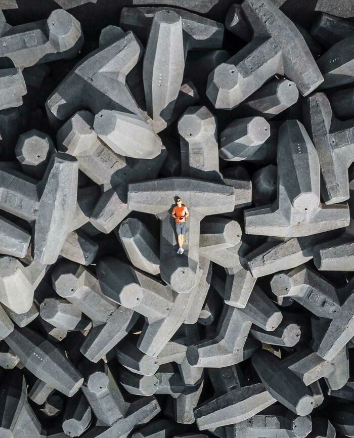 Man in orange shirt lying on large concrete blocks, showing human for scale in an unusual way.