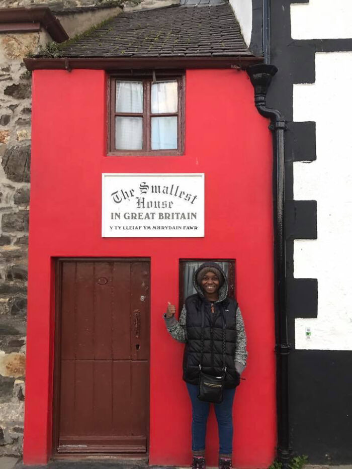 Person standing next to the smallest house in Great Britain showing human for scale with unusual size comparison.