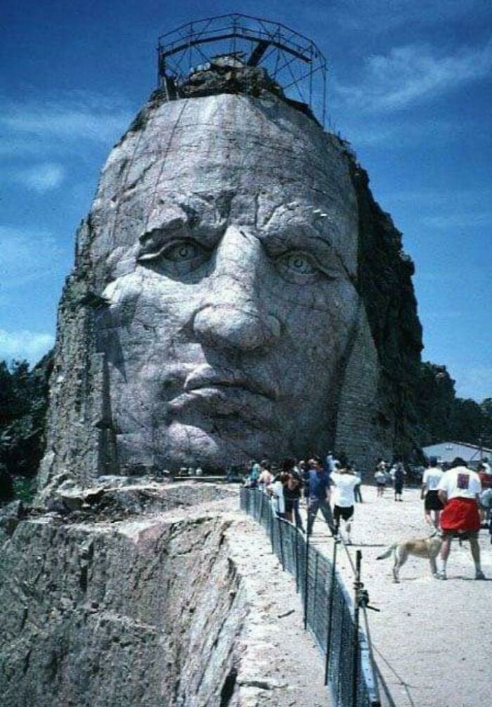 Massive stone face sculpture under construction with people nearby for human for scale showing the scale of things unusually.