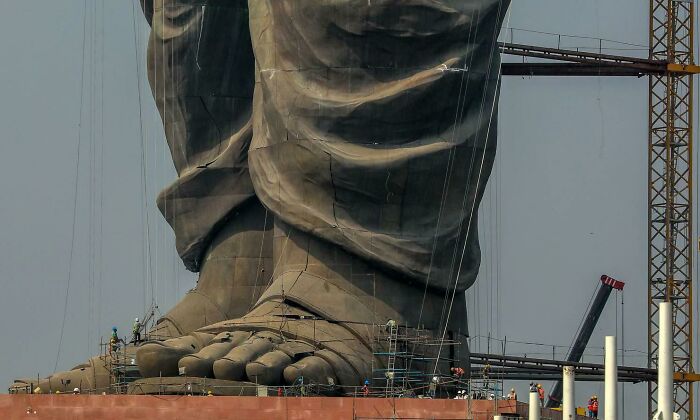 Massive statue feet under construction with workers for human for scale showing unusual size comparison.