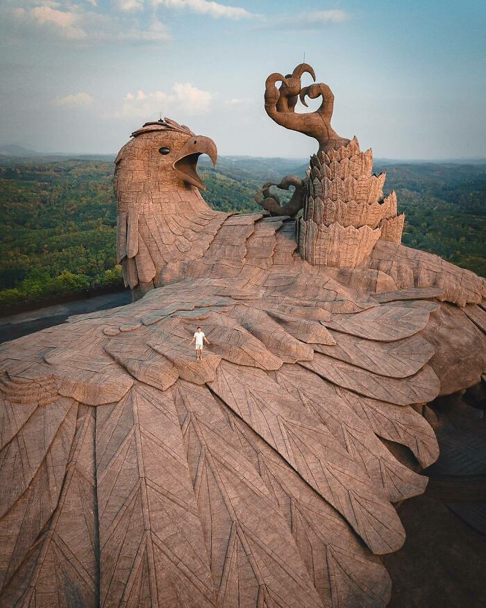 A human for scale standing on the wing of a massive eagle sculpture with detailed feathers and claws.