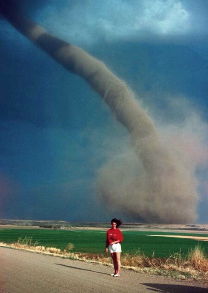 Person standing near a massive tornado showing human for scale against the powerful natural phenomenon.