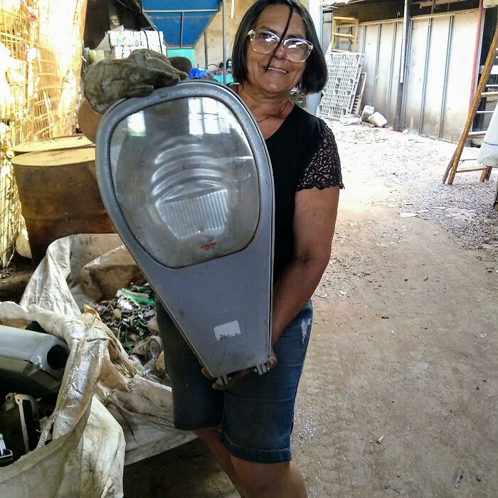 Woman holding a large vintage streetlight fixture for scale inside a workshop with tools and materials around.
