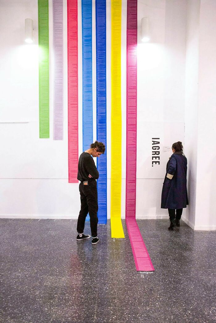 Two people standing near tall, colorful vertical strips on a wall, showing human for scale in an art gallery.