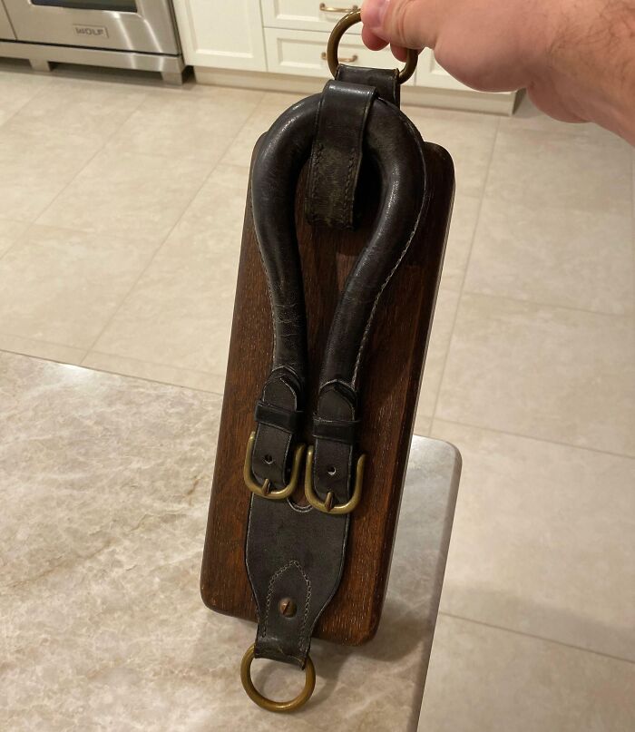 Hand holding an old leather and wood object with metal rings, a vintage find that puzzles people online.