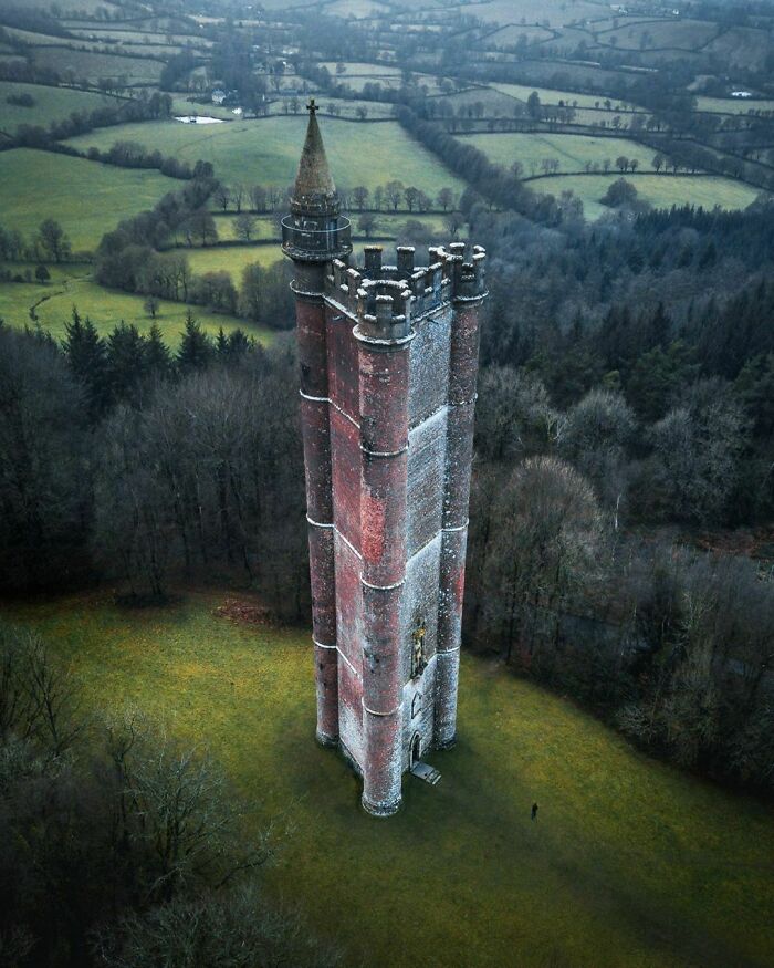 Tall historic tower in a field with a human for scale showing the size of the structure in an unusual way.