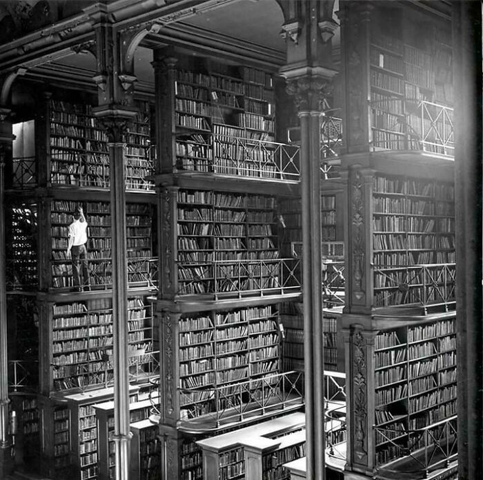 A human for scale inside a massive multi-level library filled with towering bookshelves and railings.