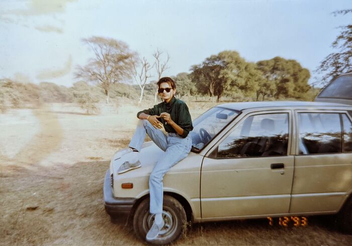 Young person wearing sunglasses sitting on the hood of a car in a vintage vacation photo before cell phone cameras existed.