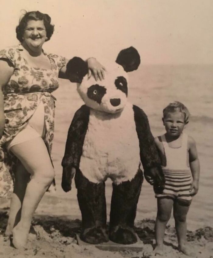 Black and white vintage vacation pic of a woman, child, and person in a panda costume on a beach.