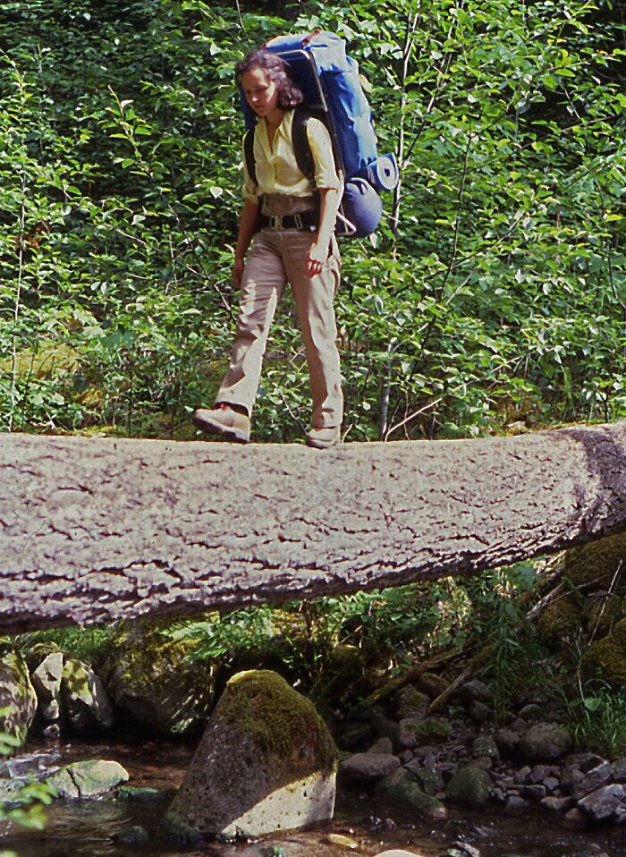 Woman with large backpack hiking over a fallen tree in the forest in a vintage vacation pic before cell phone cameras.