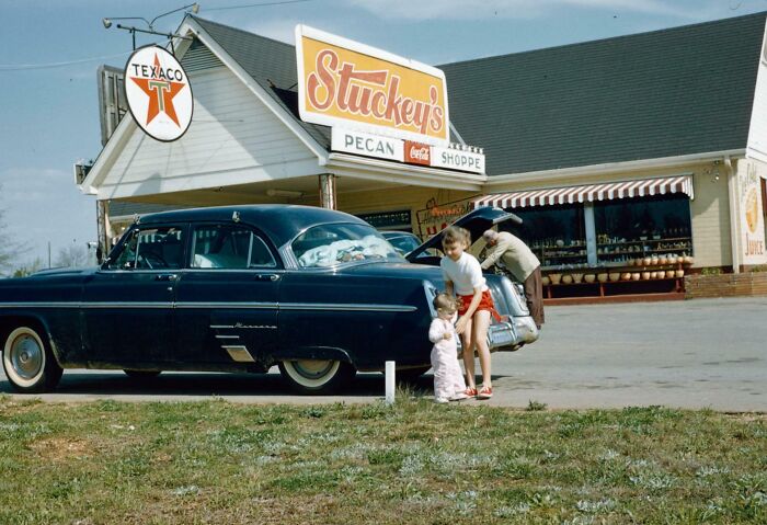 Vintage vacation scene with a classic car and family outside a roadside store, capturing a time before cell phone cameras.