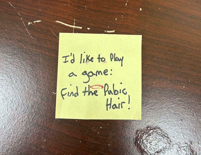 Passive-aggressive coworker note on sticky note challenging to find a misplaced hair on a wooden desk surface.
